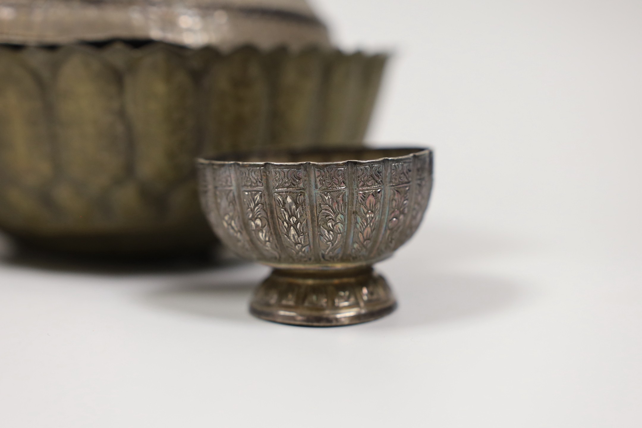 A Malay Straits pedestal bowl and cover or 'Batil Ber Tutop' (a.f.), three Malay Straits white metal betel nut cups and two similar small bowls, all with embossed floral or foliate designs (one cup with green enamelled d